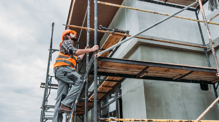 Man wearing orange high vis climbing up scaffolding